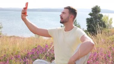 Yakışıklı adam, doğada akıllı telefonuyla selfie çekiyor.