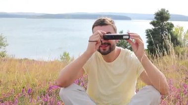 Gölün ve çiçeklerin arka planında kamerası olan yakışıklı bir fotoğrafçı.