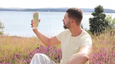 Gölün ve çiçeklerin arka planında ayna olan genç bir adam.