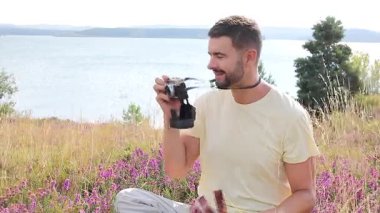 Gölün ve çiçeklerin arka planında kamerası olan yakışıklı bir fotoğrafçı.