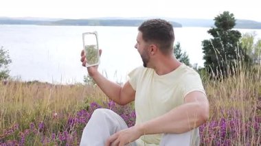 Gölün ve çiçeklerin arka planında ayna olan genç bir adam.