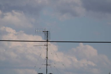 The radio antenna rises prominently against a bright sky filled with scattered clouds, creating a striking contrast during the afternoon hours. clipart