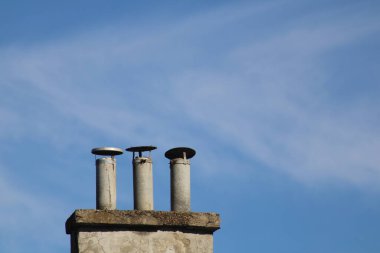 Three distinct chimneys rise from a rooftop under a bright blue sky, highlighting the architectural features of the building and the serenity of the day. clipart