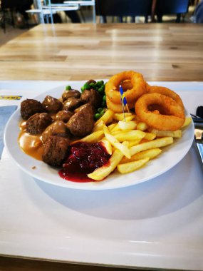 Bir tabakta tuzlu sos serpiştirilmiş köfteler, yanında kızarmış patates, soğan halkaları ve bir tutam kırmızı sos yer alıyor. Bu iştah açıcı yemek gevşemiş bir öğle yemeği için ideal..