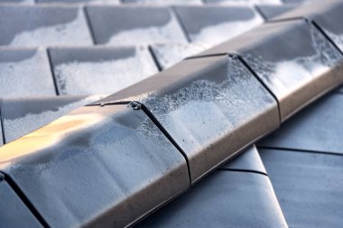 İnşaat halindeki bir binanın çatısında seramik tepeler ve fayanslar var. İlk buzun izleriyle