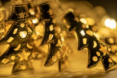 Altın Noel ağacı şeklinde parıldayan pullar ve çelenkler, süsleri ve figürleri olan, Noel konsepti. Sıcak ve lamba ortamı