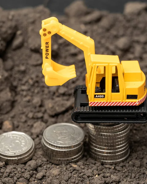 Toy model of a yellow excavator on the background of the earth with silver coins. Lean or cost building concept