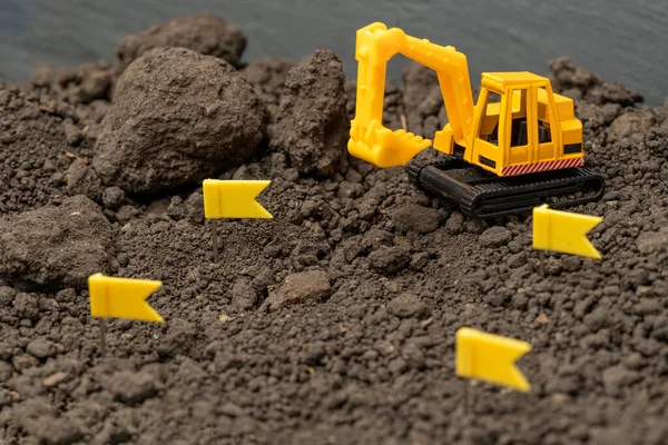 Toy model of a yellow excavator on the background of the earth with silver coins. Lean or cost building concept