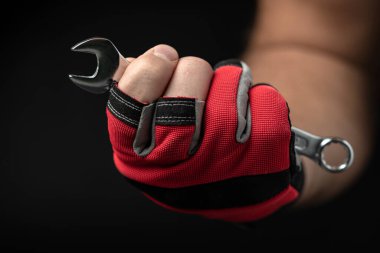 Kırmızı eldivenli güçlü bir erkek eli siyah arka planda bir ingiliz anahtarı tutuyor. Tesisat, mekanik ve otomotiv işi kavramı.