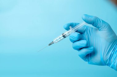 Mavi arka planda doktorun elindeki şırınga.