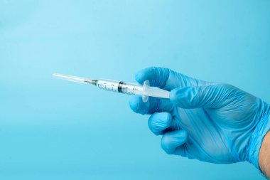 Mavi arka planda doktorun elindeki şırınga.