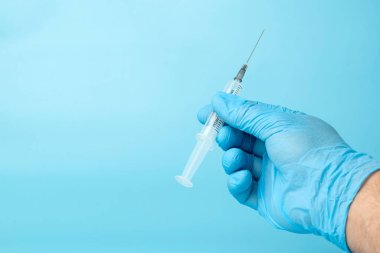 Mavi arka planda doktorun elindeki şırınga.