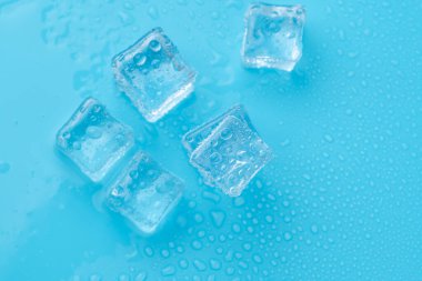 Mavi zemin üzerinde su damlaları olan buz ve buz parçaları. Soğuk ve tazelik kavramı