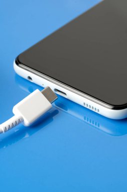 Mavi parlak arka planda bir cep telefonunu şarj etmek