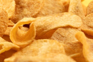 Potato chips scattered on the table close-up on a yellow background. Food with elevated cholesterol levels