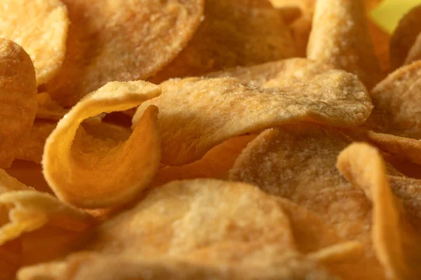 Potato chips scattered on the table close-up on a yellow background. Food with elevated cholesterol levels