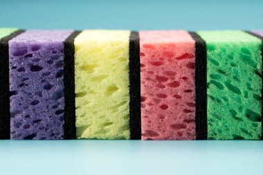 Multicolored sponges for washing dishes and other household needs. The sponges lie on a blue background at a slight angle. Cleaning and Dishwashing Concept