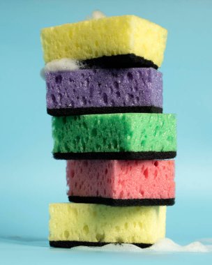 Multicolored sponges for washing dishes and other household needs. The sponges lie on a blue background at a slight angle. Cleaning and Dishwashing Concept