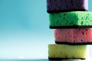 Multicolored sponges for washing dishes and other household needs. The sponges lie on a blue background at a slight angle. Cleaning and Dishwashing Concept