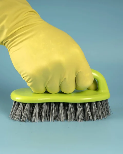 Hand in yellow rubber glove holds sponge for washing dishes and cleaning, hand clenches sponge into fist on blue background