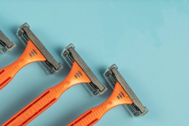Plastic razor on blue background. The concept of using a razor. Razor device. The concept of skin care. Epilation hair removal. Orange men's shaving razors, top view.