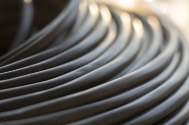 Bir rulo içinde elektrikli siyah kablo. Ağ bağlantısı, bilgisayar kablosu, kablo makarası, veri iletimi. Açık hava fabrikası deposundaki kablo makarasının silüeti.