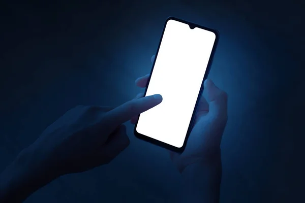 一个青少年用一只手拿着智能手机 晚上用食指触摸手机的屏幕 带有白色屏幕的手机 背景为深蓝色 文件中有一个工作路径 — 图库照片#