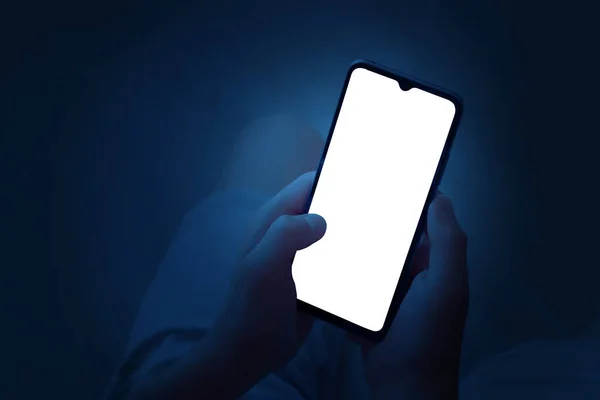 一个青少年晚上用双手拿着一部智能手机 带有白色屏幕的手机 背景为深蓝色 文件中有一个工作路径 — 图库照片#