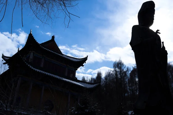 Winter in the morning in a old temple of an old town in Jiamusi, city of china, visible moon in background blue sky. pagoda snow cover, Budda statue and blue sky behind.