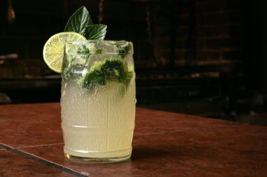 Buzlu kristal bardakta taze yapraklarla mojito kokteyli. Taze limon dilimleri, karanlık bir masanın üzerinde. 