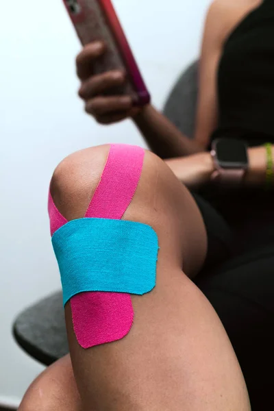 female therapist applying kinesiology taping to the knee and leg of a latina patient on a black stretcher in a physical rehabilitation clinic.