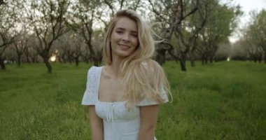 Beyaz elbiseli çarpıcı bir kadın zarif bir şekilde yeşil bir meyve bahçesinde duruyor, güzelliği yakalıyor..