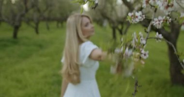 Huzurlu bir bahar bahçesinde duran genç bir kadın etrafındaki güzel çiçeklere hayran.