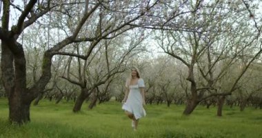 Bir kadın, bahar mevsiminin sakin bir sahnesine dalmış güzel çiçek açan bir meyve bahçesinde zarifçe dolaşır.