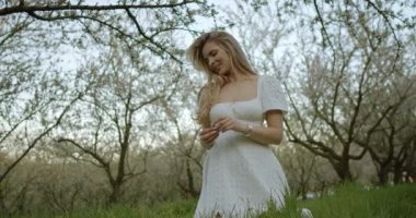 Işıldayan genç bir kadın, çiçek açan ağaçlarla çevrili doğanın güzelliğine dalmış huzurlu bir anın tadını çıkarıyor.