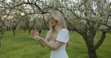 Genç bir kadın, göz kamaştırıcı bir meyve bahçesinde çiçek açan ağaçlarla çevrili harika ve huzurlu bir anın tadını çıkarıyor.