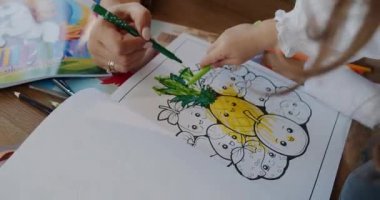 Bir çocuk neşeli ve renkli bir şekilde yaratıcı bir aktiviteye katılır, bir ananas karakterini pastel kalemlerle canlandırır.