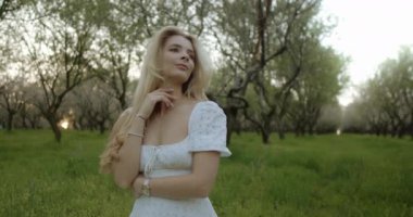 Göz kamaştırıcı bir kadın, bahar zamanı çiçeklerle dolu yemyeşil bir meyve bahçesinde zarifçe poz verir.
