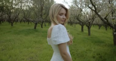 Akan beyaz elbiseli genç bir kadın canlı bir meyve bahçesinde huzur içinde duruyor, doğanın güzelliğini kucaklıyor.