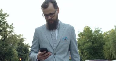 İyi giyimli bir adam, hayat dolu trendli bir şehir ortamında güvenli bir şekilde yürürken akıllı telefonunu kontrol eder.