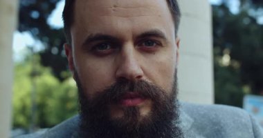 Açık havada sakallı bir adamın yakın plan portresi, yüzündeki düşünceli ifadeyi doğal ışık altında yakalıyor.