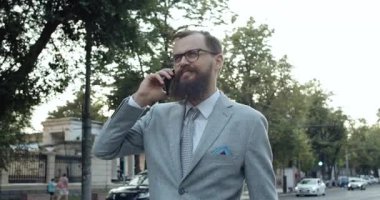 Şık ve kendine güvenen bir işadamı, işlek bir caddede yürürken cep telefonuyla konuşuyor.