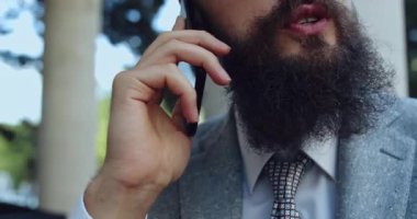 Sivri takım elbiseli profesyonel bir adam telefonuyla konuşuyor, modern bir iş ortamının altını çiziyor.