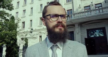 Şık sakallı ve şık gözlüklü şık bir işadamı modern bir binanın önünde duruyor.