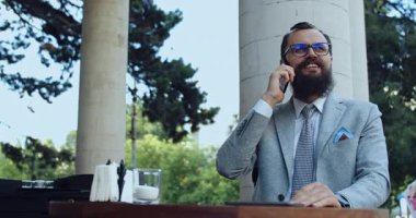 Şık takım elbiseli iyi giyimli bir adam dışarıdaki bir telefon görüşmesinde canlı bir iş ortamını yansıtıyor.