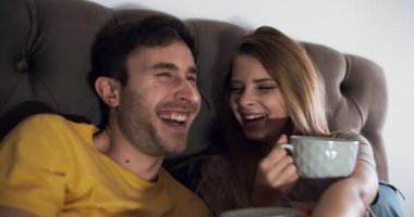 Neşeli bir çift, rahat bir kanepede dinlenirken kahkaha ve kahveyle dolu sıcak bir anın tadını çıkarır.