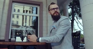 Şık bir kafede, iyi giyimli bir adam zarif bir ortamda telefonuna tamamen dalmış.