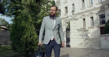 Şık sakallı bir adam büyük bir binanın etrafında rahatça dolaşıyor, göz alıcı bir cazibe, zarafet ve klas.