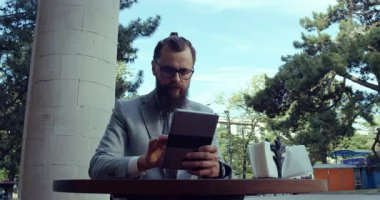 Tarz sahibi bir işadamı antika bir kafede, tabletini kullanıyor ve modern iş hayatı dengesini gösteriyor.