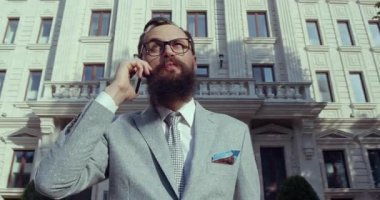 Kusursuz giyimli şık bir işadamı zarif bir binanın dışında bir telefon görüşmesi yapıyor.